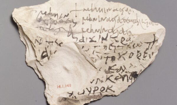 a roughly triangular chunk of sand-coloured stone, with almost indecipherable ancient greek writing scrawled across some faces. A large flat chip is missing from one section, on which is stamped an aquisition number, 14.1.140